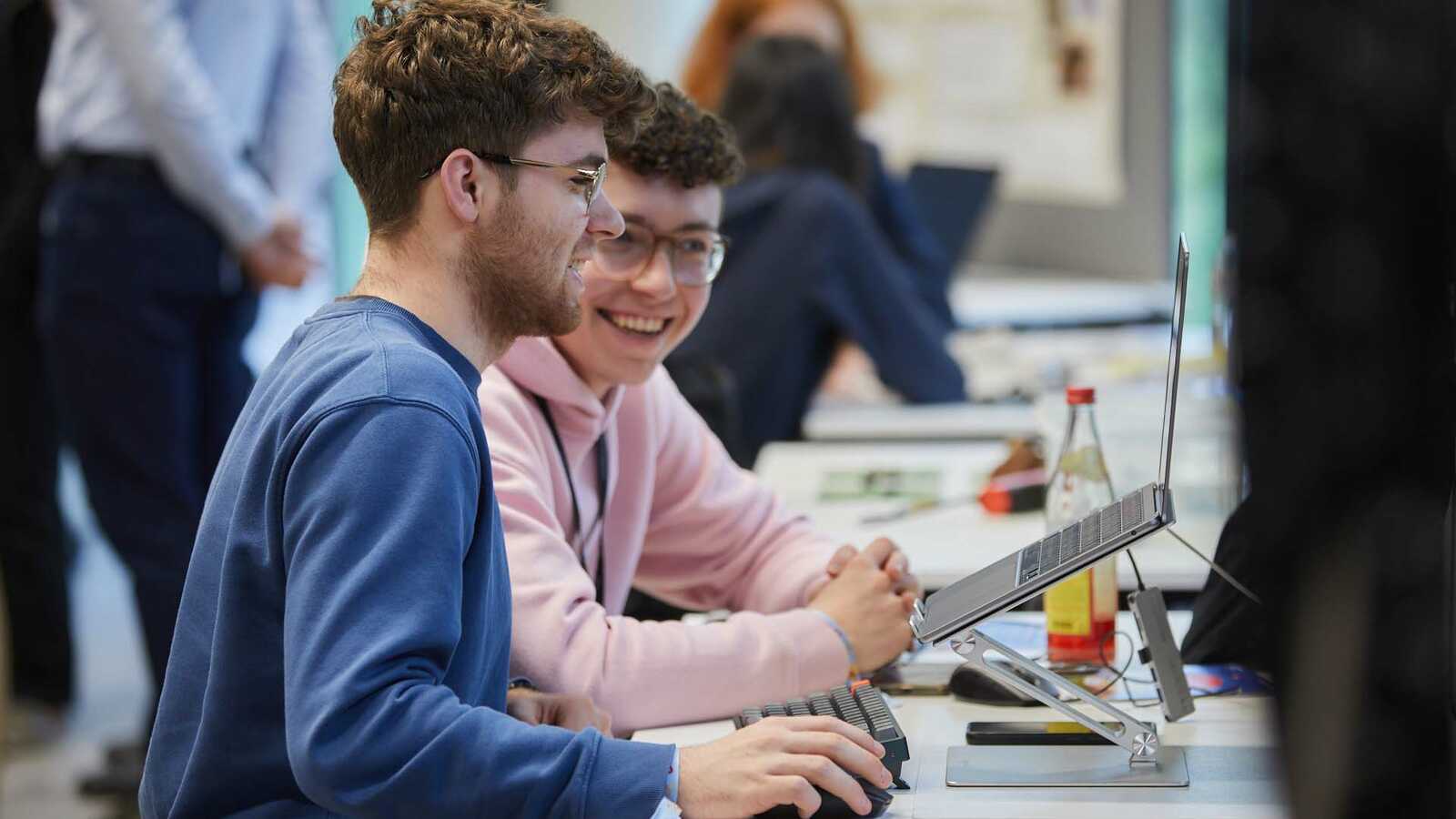 Zwei Jungforschende lachend an einem Laptop