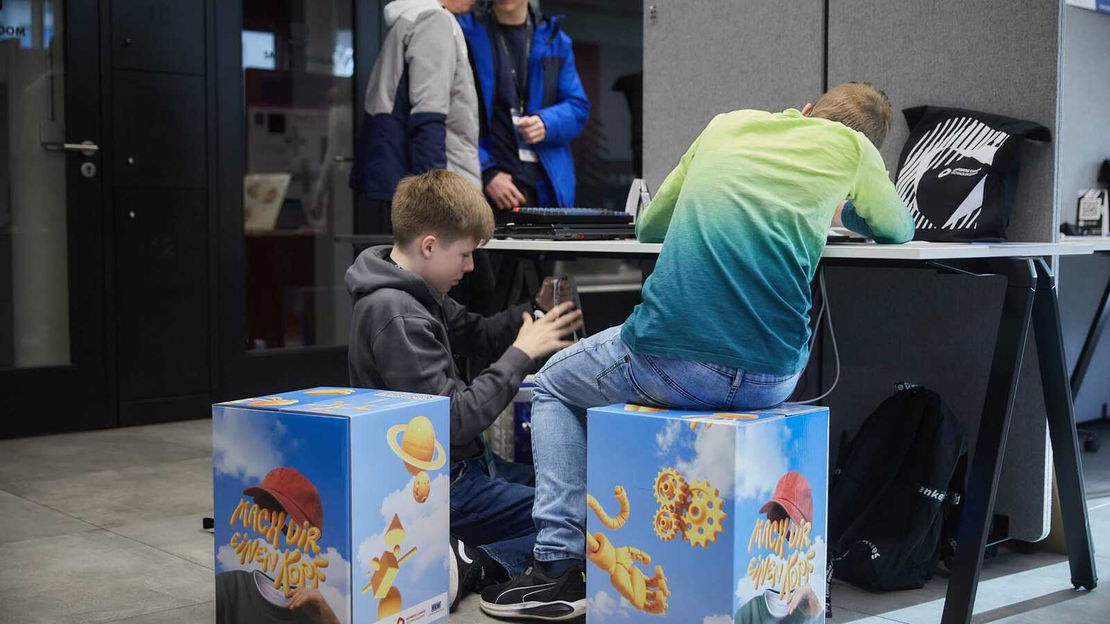 Zwei Jungforschende auf Hockern sitzend von hinten