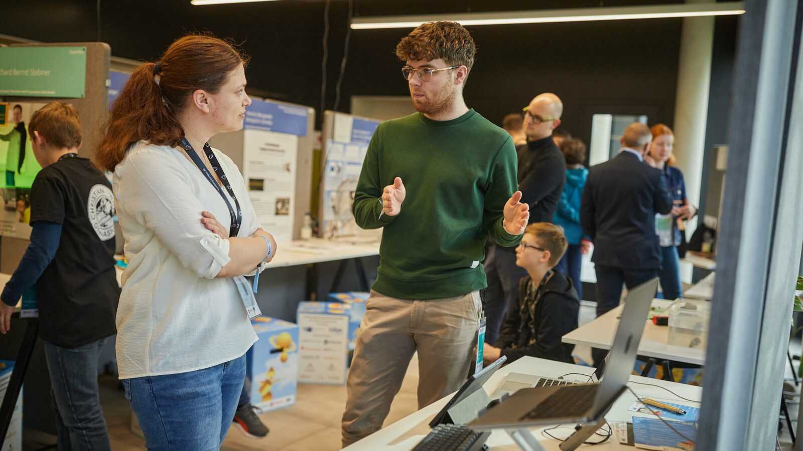 Menschen und Jungforschende an Ständen der Ausstellung im Gespräch