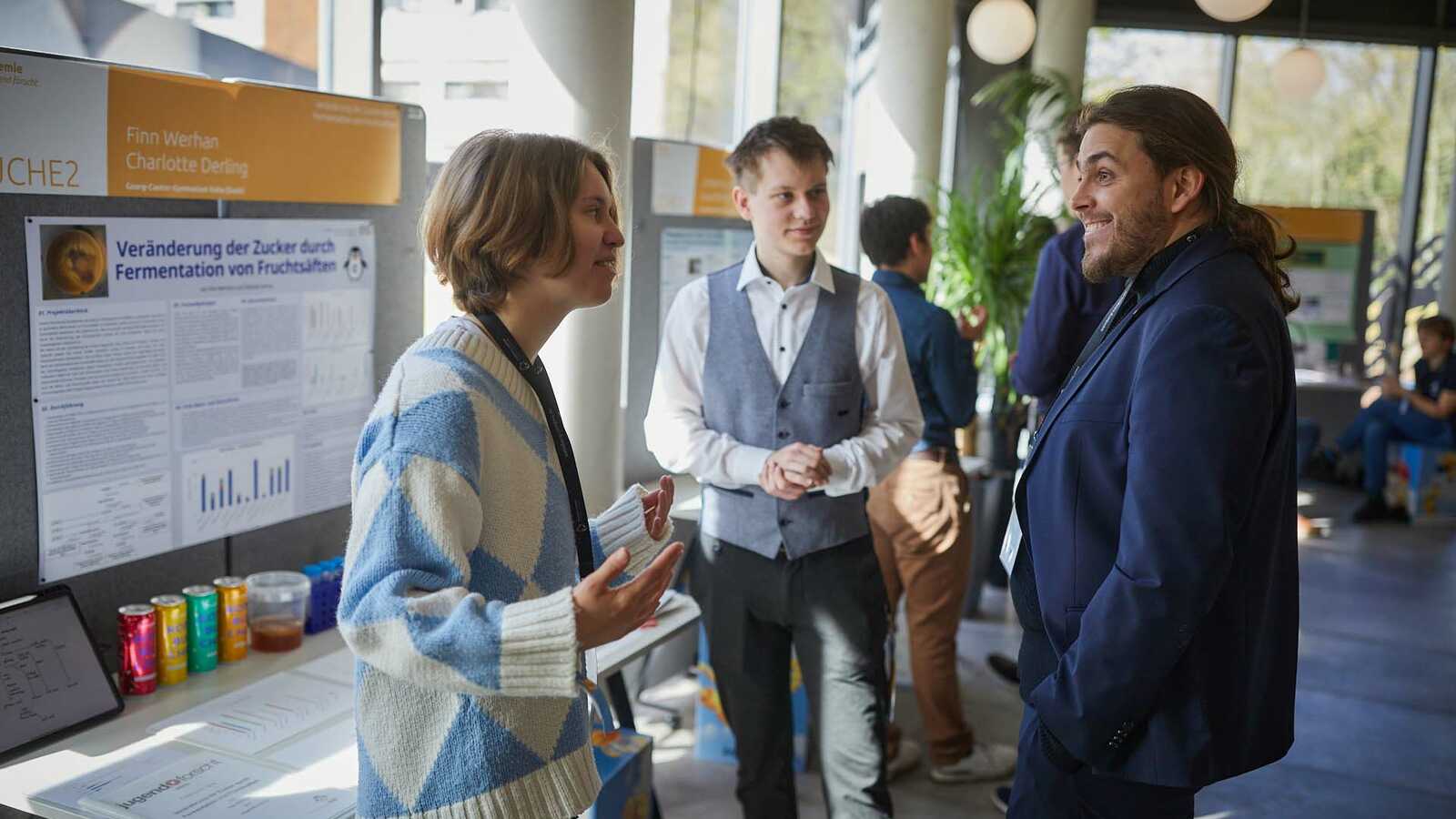 Menschen und Jungforschende an Ständen der Ausstellung im Gespräch