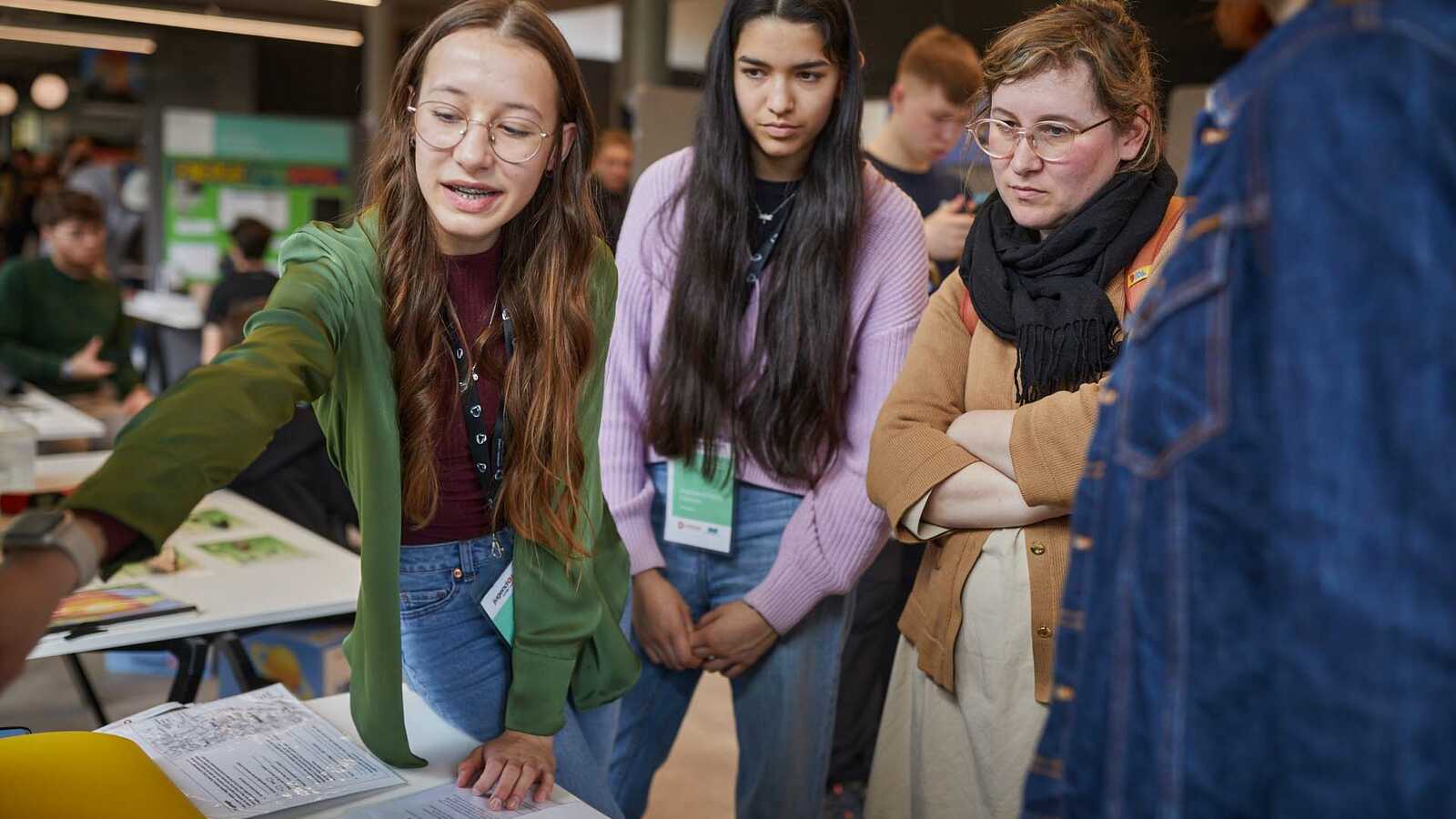 Menschen und Jungforschende an Ständen der Ausstellung im Gespräch