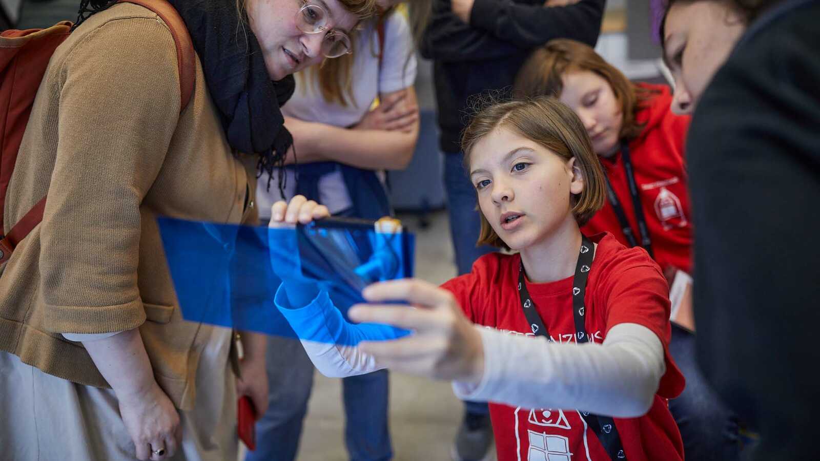 Jungforschende zeigt einen Gegenstand gegen eine blaue Folie